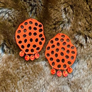 May include: A pair of orange statement earrings with a honeycomb pattern and dangling orange and red beads.
