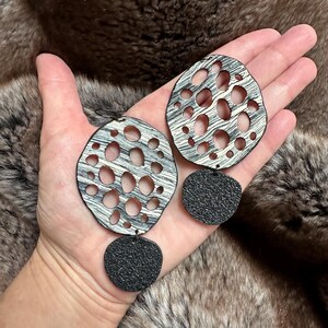 May include: A pair of silver and black earrings with a geometric design. The earrings are made of two pieces, a larger circle with cutouts and a smaller circle.
