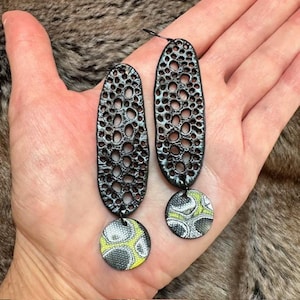 May include: Black dangle earrings with a geometric pattern and a round, black and white patterned charm.
