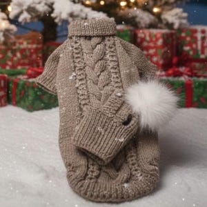 Könnte beinhalten: Ein brauner Zopfstrick-Hundepullover mit passendem Ärmel und einem weißen Kunstfell-Pompon. Der Pullover hat einen Rollkragen und ist mit kleinen weißen Akzenten verziert, vor einem verschneiten Hintergrund mit Weihnachtsgeschenken.