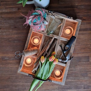 Könnte beinhalten: Ein Holztablett mit Fächern, gefüllt mit verschiedenen Gegenständen, darunter Kerzen, eine Glasvase, ein Seil, Stöcke und Blumen. Das Tablett hat einen rustikalen, ländlichen Stil.