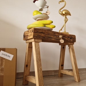 Könnte beinhalten: Ein rustikaler Holzschemel mit einem Stapel Obst und Tellern, gekrönt von einer Tasse Trauben. Eine goldene Flamingostatue steht daneben. Ein Karton mit dem Wort "zeitliebe" befindet sich links.