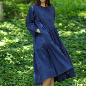 Puede incluir: Vestido largo azul marino con cuello redondo y mangas largas. El vestido tiene una falda escalonada y se usa con sandalias negras. El fondo es un bosque verde. El vestido mide aproximadamente 130 cm de largo.