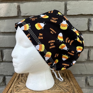 May include: Black scrub hat with a Halloween candy corn pattern. The candy corn has a face and says "I'm corny", "Bite me", and "Trick or Treat".