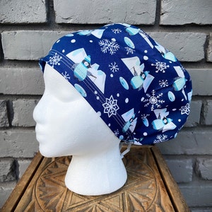 May include: A blue and white patterned scrub hat with a winter theme. The hat features penguins, snowflakes, and a white background.