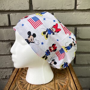 May include: A gray and white scrub hat with a red, white, and blue American flag, stars, and Mickey Mouse characters.
