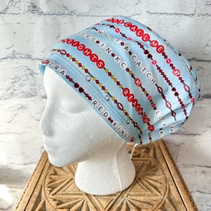 May include: A light blue surgical scrub hat with a pattern of red and white beads, footballs, and the text "13-CALL-ME 8700", "VERSINK C8740LER", "WHAT A CATCH", "DERARED KINGDOM", "HEIGHTS-REACHNEW I", "K", "A".