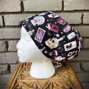 May include: A black and white patterned surgical scrub hat with a skull, stars, and the words "Magic Spells".