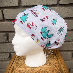 May include: A gray and white scrub hat with a Christmas theme featuring cartoon characters and trees. The hat has a tie string.