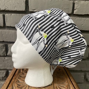 May include: Black and white striped scrub hat with a repeated pattern of a skeleton figure with the text "This is Halloween" on a banner.