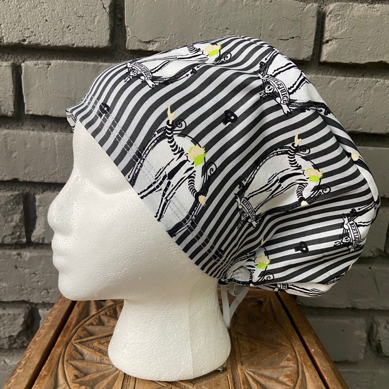 May include: Black and white striped scrub hat with a repeated pattern of a skeleton figure with the text "This is Halloween" on a banner.
