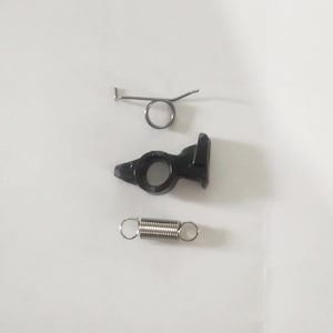 Puede incluir: Tres piezas metálicas para un dispositivo mecánico. Una pieza de plástico negro con un pequeño agujero y un gancho metálico, un resorte plateado y un resorte plateado con un gancho.