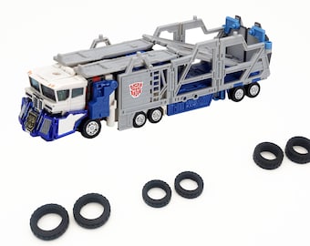 May include: A blue and white toy truck with a gray trailer. The trailer has a ramp and is designed to carry other vehicles. The truck has a  "Transformers" logo on the side. The truck is missing some of its tires, which are shown separately.