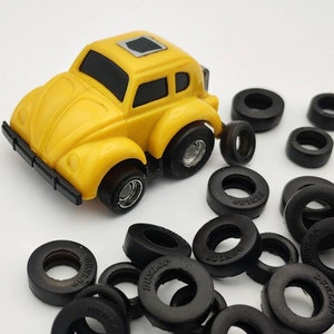 May include: A yellow toy car shaped like a Volkswagen Beetle with black tires and a black sunroof. The car is surrounded by black rubber rings with the word "Dunlop" printed on them.