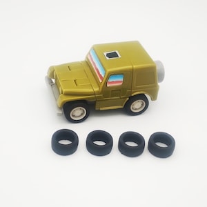 May include: A gold toy jeep with a spare tire and four separate black tires. The jeep has a white front bumper, white wheels, and colorful window details. The toy is on a white background.