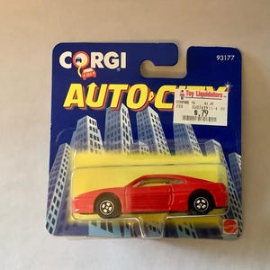 May include: A red Corgi Auto City toy car in its original packaging. The packaging is blue with a cityscape design and the words "CORGI" and "AUTO CITY" in yellow. The car is a Ferrari model.