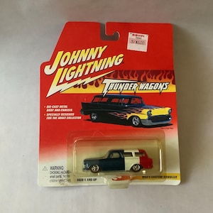 May include: A Johnny Lightning die-cast metal toy car on a red and yellow card. The car is a custom wagon with a navy blue, white, and red color scheme. The card reads "Thunder Wagons" and "Ages 6 and up."