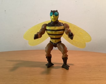 May include: A vintage action figure of a bee-like creature with yellow wings, a brown body, and a black and yellow striped chest. The figure has a menacing expression and is posed with its wings spread.