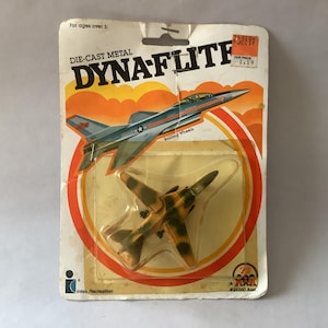 May include: Vintage Dynaflite die-cast metal toy airplane in original packaging. The packaging features a graphic of a blue and gray jet plane with orange and yellow accents. The toy plane inside is yellow and brown.