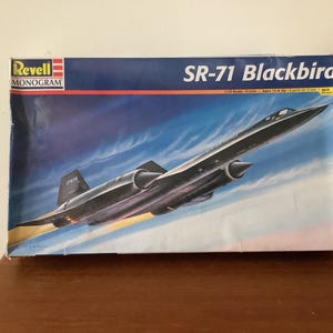 Puede incluir: Caja de modelo del avión SR-71 Blackbird. La caja presenta una ilustración detallada del avión a reacción negro sobre un fondo de cielo azul. El logotipo de Revell Monogram es visible en la esquina superior izquierda.