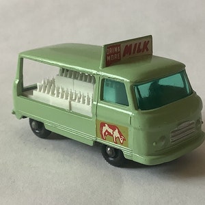 Puede incluir: Una camioneta de reparto de leche de juguete verde con techo blanco y un letrero que dice "Drink More Milk". La camioneta lleva una carga completa de botellas de leche blancas.