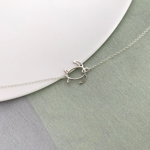 Peut inclure: Un collier en chaîne argent avec un pendentif délicat en forme de tortue. La tortue est faite de métal fin et a un design simple et élégant.