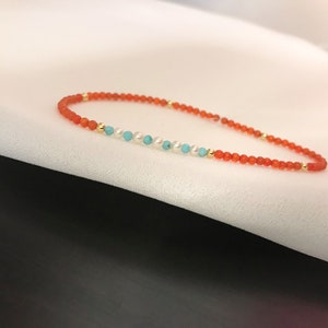 May include: A delicate bracelet with small orange beads, interspersed with turquoise and white beads, and gold accents. The bracelet is strung on a thin cord, creating a minimalist design. A stylish accessory for everyday wear, suitable for any occasion.