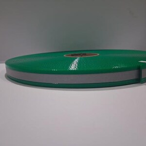 Puede incluir: Un rollo de cinta reflectante verde con una franja reflectante gris. La cinta est&aacute; enrollada y asegurada con una banda blanca. La cinta est&aacute; dise&ntilde;ada para la seguridad y la visibilidad.