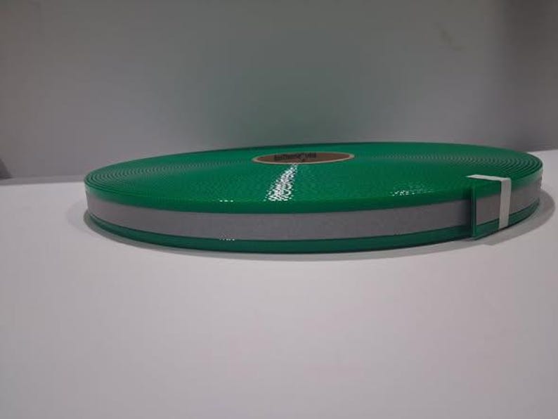 Puede incluir: Un rollo de cinta reflectante verde con una franja reflectante gris. La cinta est&aacute; enrollada y asegurada con una banda blanca. La cinta est&aacute; dise&ntilde;ada para la seguridad y la visibilidad.