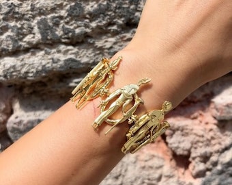 May include: Gold bracelet with a design of multiple figures, possibly Egyptian in style.