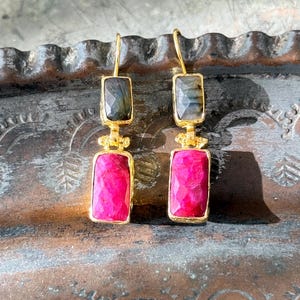May include: Gold dangle earrings with a pink and gray gemstone design.