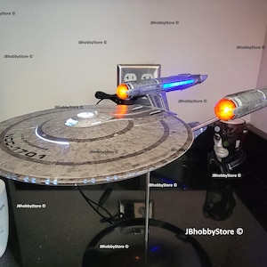 K&ouml;nnte beinhalten: Detailliertes Modell der Star Trek USS Enterprise NCC-1701, mit beleuchteten Gondeln und Untertassensektion. Das Modell ist auf einem St&auml;nder montiert, mit einer wei&szlig;en Tasse im Vordergrund. Sammlerst&uuml;ck.
