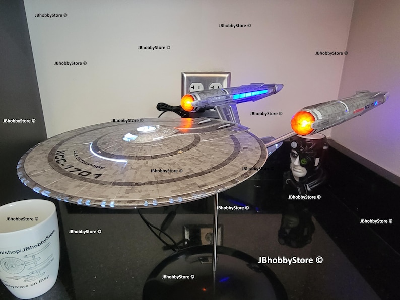 K&ouml;nnte beinhalten: Detailliertes Modell der Star Trek USS Enterprise NCC-1701, mit beleuchteten Gondeln und Untertassensektion. Das Modell ist auf einem St&auml;nder montiert, mit einer wei&szlig;en Tasse im Vordergrund. Sammlerst&uuml;ck.
