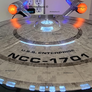 K&ouml;nnte beinhalten: Ein detailliertes Modell der U.S.S. Enterprise NCC-1701, einem Raumschiff aus der Star Trek-Serie. Das Modell ist grau mit schwarzer Schrift und beleuchteten blauen und orangefarbenen Lichtern. Der Text "U.S.S. Enterprise NCC-1701" ist sichtbar.