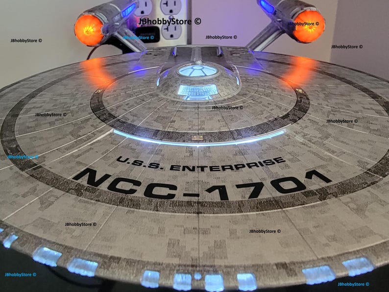 K&ouml;nnte beinhalten: Ein detailliertes Modell der U.S.S. Enterprise NCC-1701, einem Raumschiff aus der Star Trek-Serie. Das Modell ist grau mit schwarzer Schrift und beleuchteten blauen und orangefarbenen Lichtern. Der Text "U.S.S. Enterprise NCC-1701" ist sichtbar.