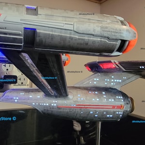 K&ouml;nnte beinhalten: Zwei detaillierte Modellraumschiffe, eines &uuml;ber dem anderen, mit beleuchteten Fenstern und Triebwerkslichtern. Das obere Schiff hat eine orangefarbene Front, w&auml;hrend das untere Schiff ein rotes Heck hat. Die Modelle sind grau und schwarz, mit dem Text "JBhobbyStore &copy;" sichtbar.