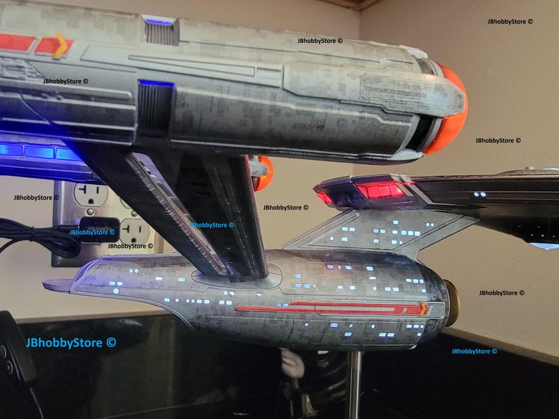 K&ouml;nnte beinhalten: Zwei detaillierte Modellraumschiffe, eines &uuml;ber dem anderen, mit beleuchteten Fenstern und Triebwerkslichtern. Das obere Schiff hat eine orangefarbene Front, w&auml;hrend das untere Schiff ein rotes Heck hat. Die Modelle sind grau und schwarz, mit dem Text "JBhobbyStore &copy;" sichtbar.