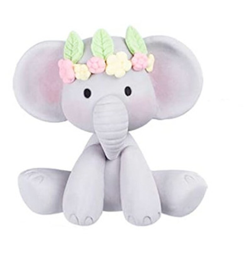 Puede incluir: Una figurita de elefante gris que lleva una corona de flores con flores rosas, amarillas y verdes. El elefante est&aacute; sentado con las piernas cruzadas y tiene una expresi&oacute;n dulce en su rostro.