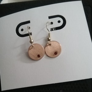 May include: A pair of copper earrings with a small red gemstone in the center of each disc.