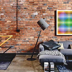 May include: A living room with a brick wall, a gray sectional sofa, a floor lamp, and a colorful abstract artwork hanging on the wall.