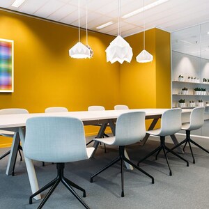May include: A white rectangular table with six white chairs sits in a meeting room with a yellow wall. Three white pendant lights hang from the ceiling. A colorful abstract artwork hangs on the wall.