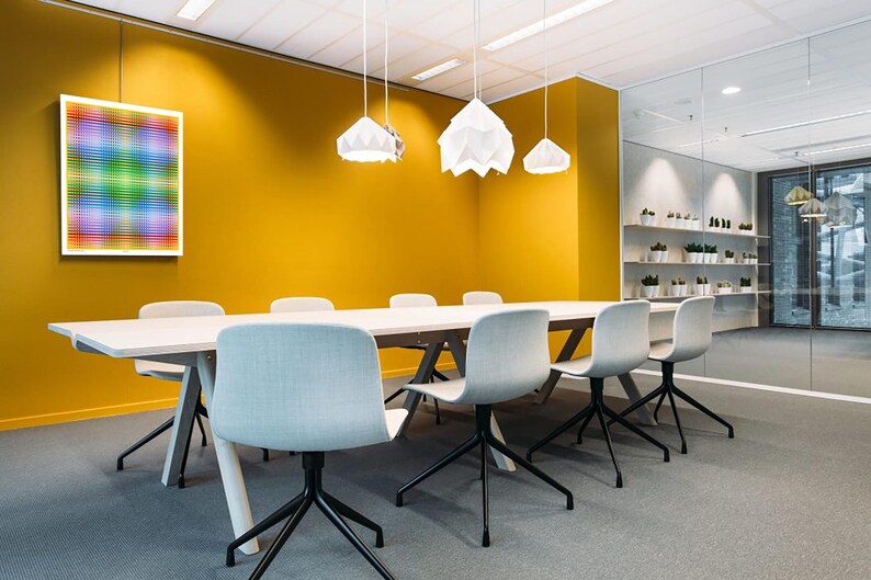 May include: A white rectangular table with six white chairs sits in a meeting room with a yellow wall. Three white pendant lights hang from the ceiling. A colorful abstract artwork hangs on the wall.