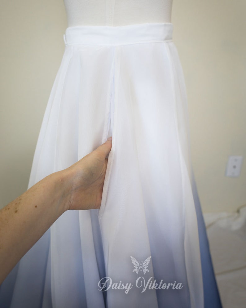 May include: A white and blue ombre maxi skirt with a white waistband and a single pleat in the front. The skirt is made of a soft, flowing fabric and has a subtle ombre effect that transitions from white to blue.