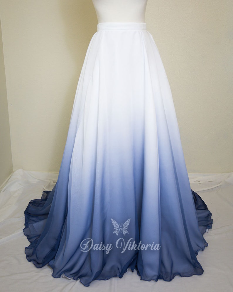 May include: A long white and blue ombre chiffon skirt with a high waist. The skirt is gathered at the waist and flows down to a ruffled hem. The skirt is a light blue color at the bottom and fades to white at the top. The skirt is made of a soft, flowing fabric. The skirt is perfect for a special occasion or for everyday wear.