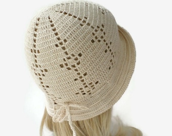 May include: A crocheted hat with a delicate openwork design in a cream color. The hat has a wide brim and a bow at the back.