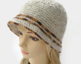 Puede incluir: Un sombrero cloche beige con un diseño de punto texturizado. El ala presenta dos rayas marrones y naranjas. El sombrero se muestra en una cabeza de maniquí con cabello rubio.