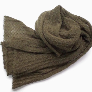 May include: An olive green scarf made of a soft, textured material. The scarf is draped and folded, showcasing its length and the intricate weave. The color is a muted, earthy tone, suitable for various outfits.