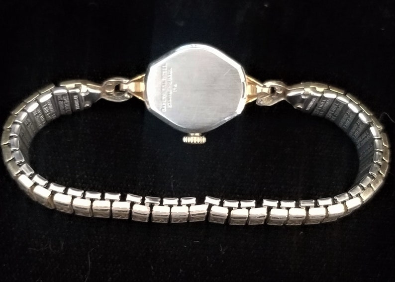 K&ouml;nnte beinhalten: Eine silberne und goldene Armbanduhr mit einem silbernen Armband. Das Zifferblatt der Uhr ist achteckig und hat einen silbernen R&uuml;cken.