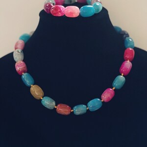 Pu&ograve; includere: Un set di collana e braccialetto in pietra di agata multicolore. La collana e il braccialetto sono realizzati con perline ovali in tonalit&agrave; di rosa, blu e marrone.