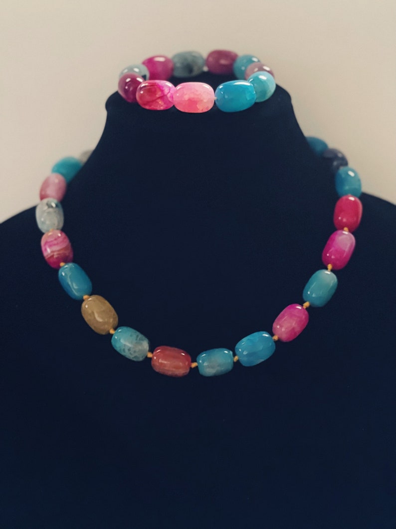 Pu&ograve; includere: Un set di collana e braccialetto in pietra di agata multicolore. La collana e il braccialetto sono realizzati con perline ovali in tonalit&agrave; di rosa, blu e marrone.